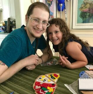 Rhys and a young girl with long curly hair sitting at a table, leaning together and smiling.