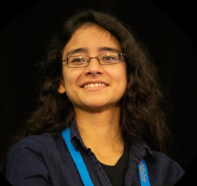Angie is a woman with long wavy brown hair and glasses. She is looking toward the camera and smiling.